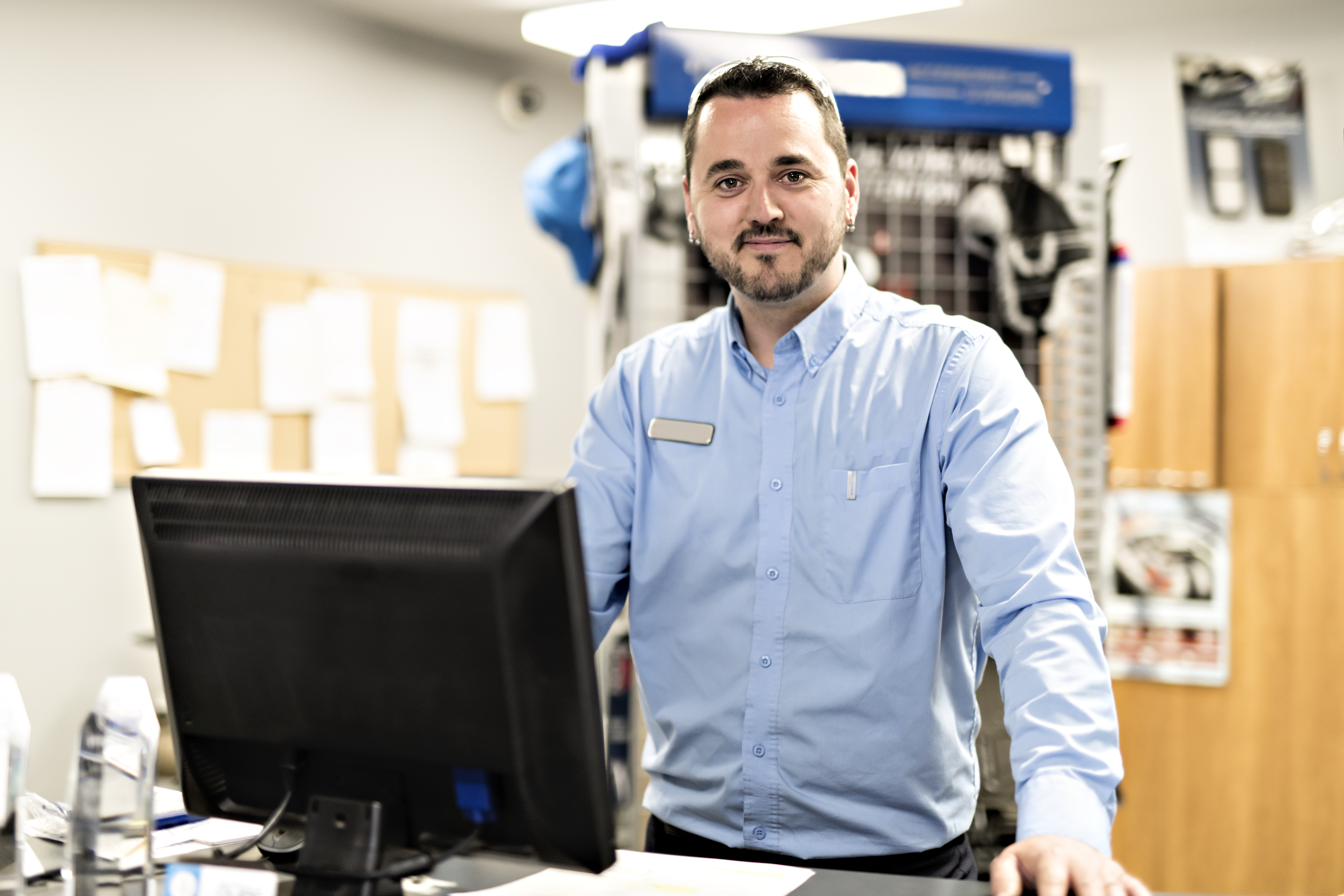 Picture of a smiling nechanic stood at a reception desk
